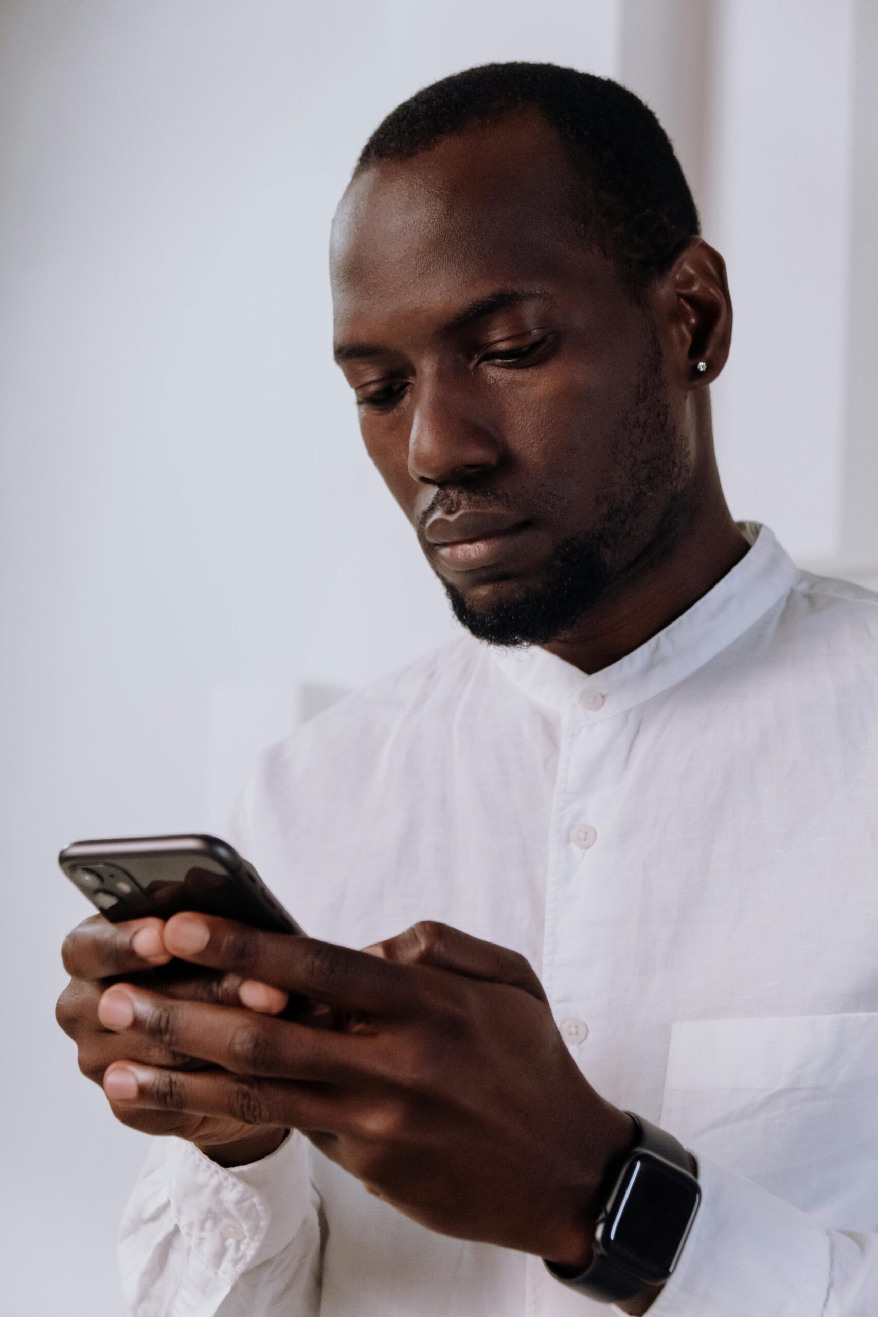 Confident man in white shirt using smartphone, wearing modern smartwatch in an office setting.