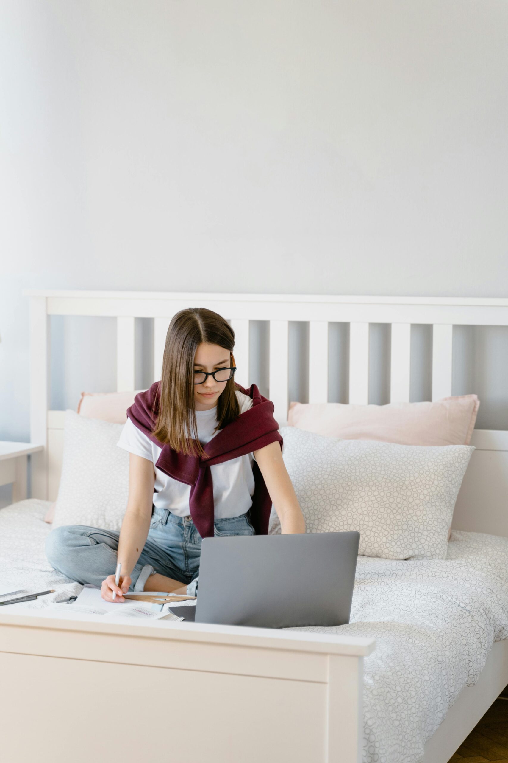Woman sitting on bed with laptop, participating in remote learning session indoors.